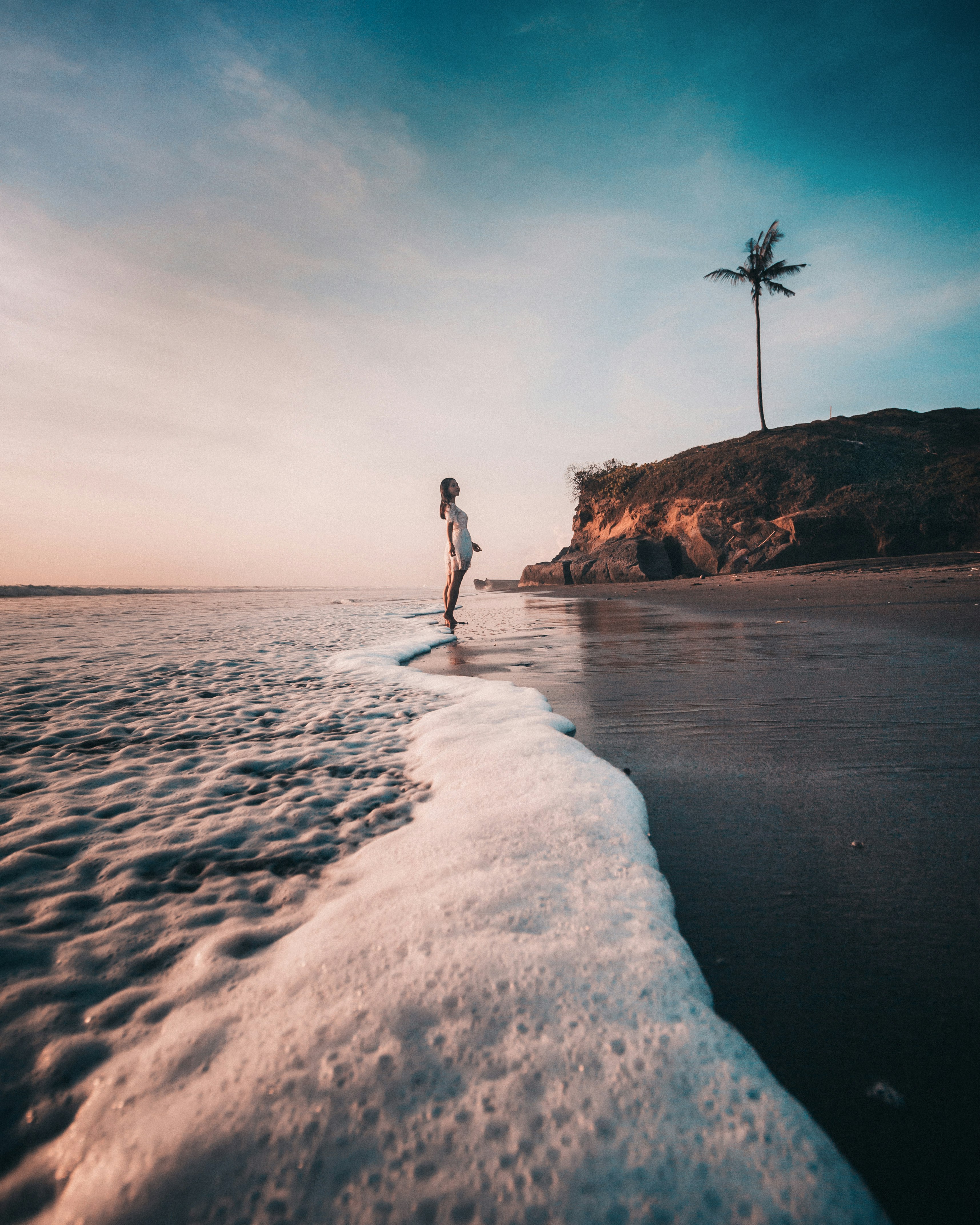 woman in white shirt and black pants standing on white sand beach during daytime